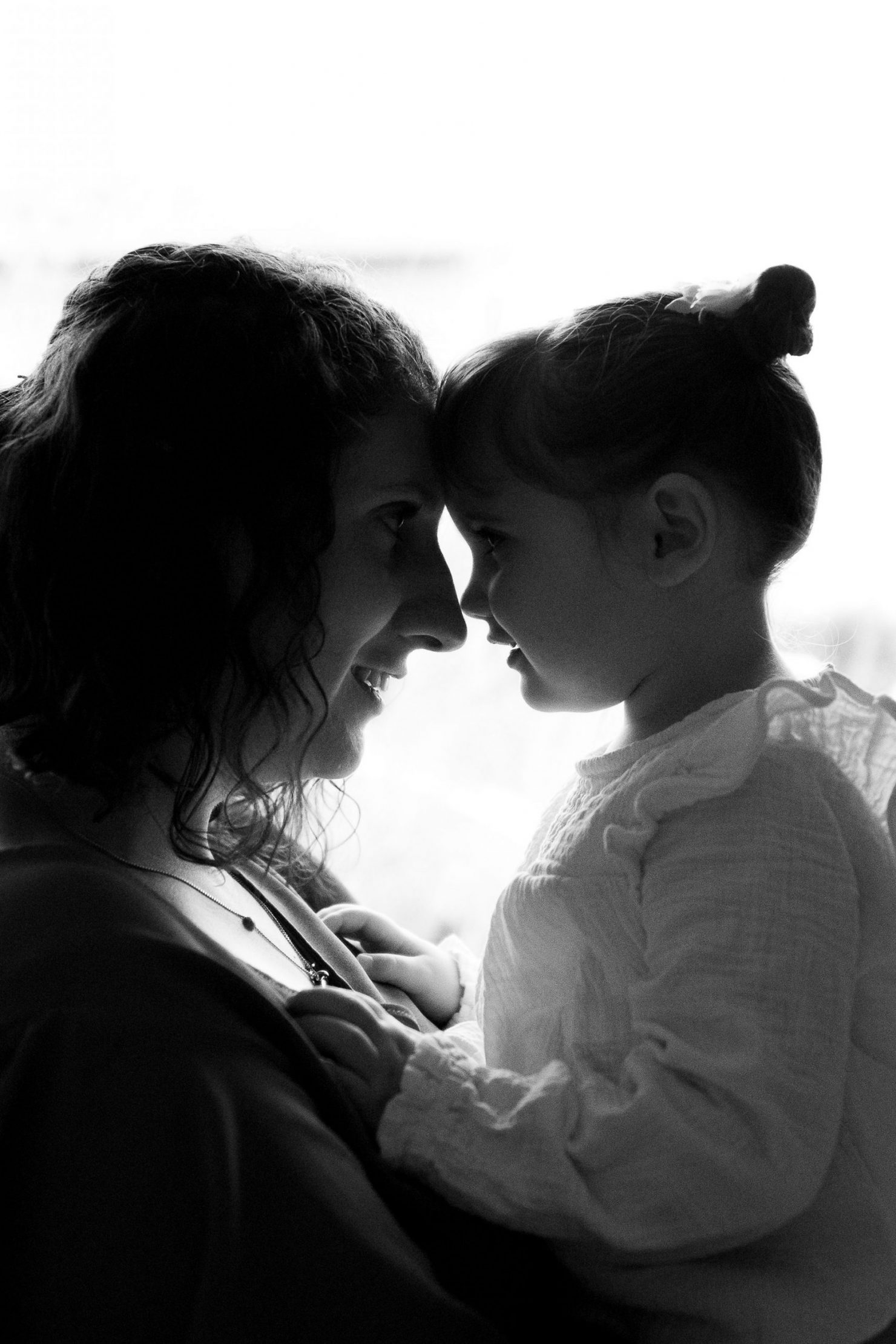 Une maman et son enfant sont front contre front en contre-jour pendant leur séance photo famille. Une photo silhouette créée par Meyline Esparcieux, photographe Dax.