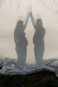 La silhouette d'une femme enceinte et de son chéri en silhouette en contre-jour sur un drap. Une photo créative créée par Meyline Esparcieux, photographe Dax.