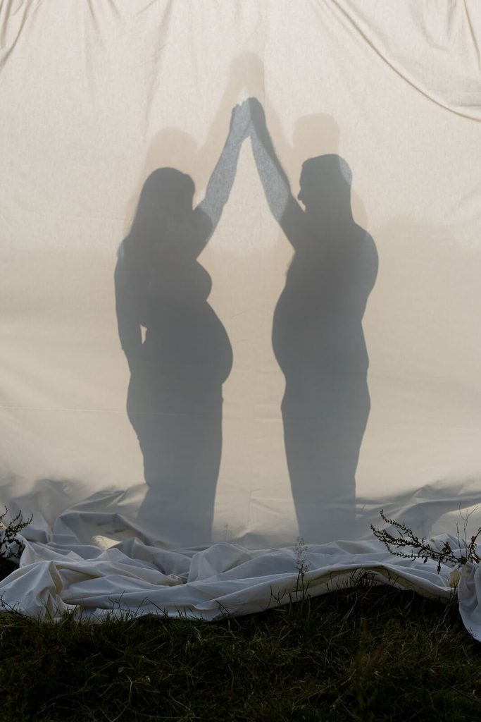 La silhouette d'une femme enceinte et de son chéri en silhouette en contre-jour sur un drap. Une photo créative créée par Meyline Esparcieux, photographe Dax.