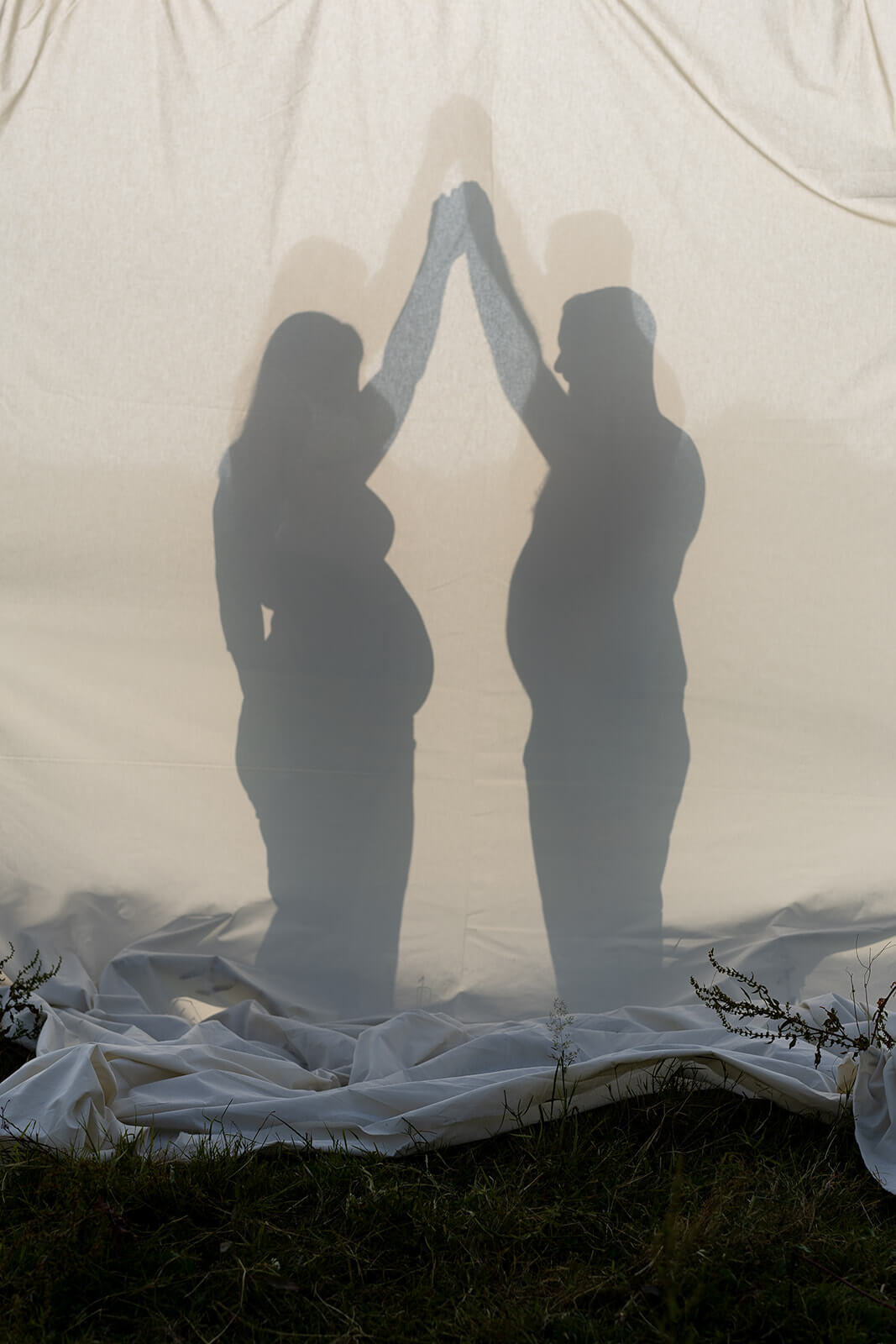 La silhouette d'une femme enceinte et de son chéri en silhouette en contre-jour sur un drap. Une photo créative créée par Meyline Esparcieux, photographe Dax.
