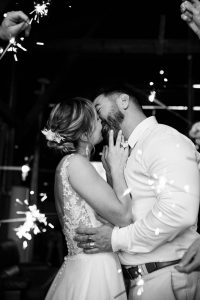 Le couple de mariés s'embrasse pendant leur soirée de mariage pendant que leurs invités tiennent des cierges étincelants. Un moment magique saisi par Meyline Esparcieux, photographe Dax.