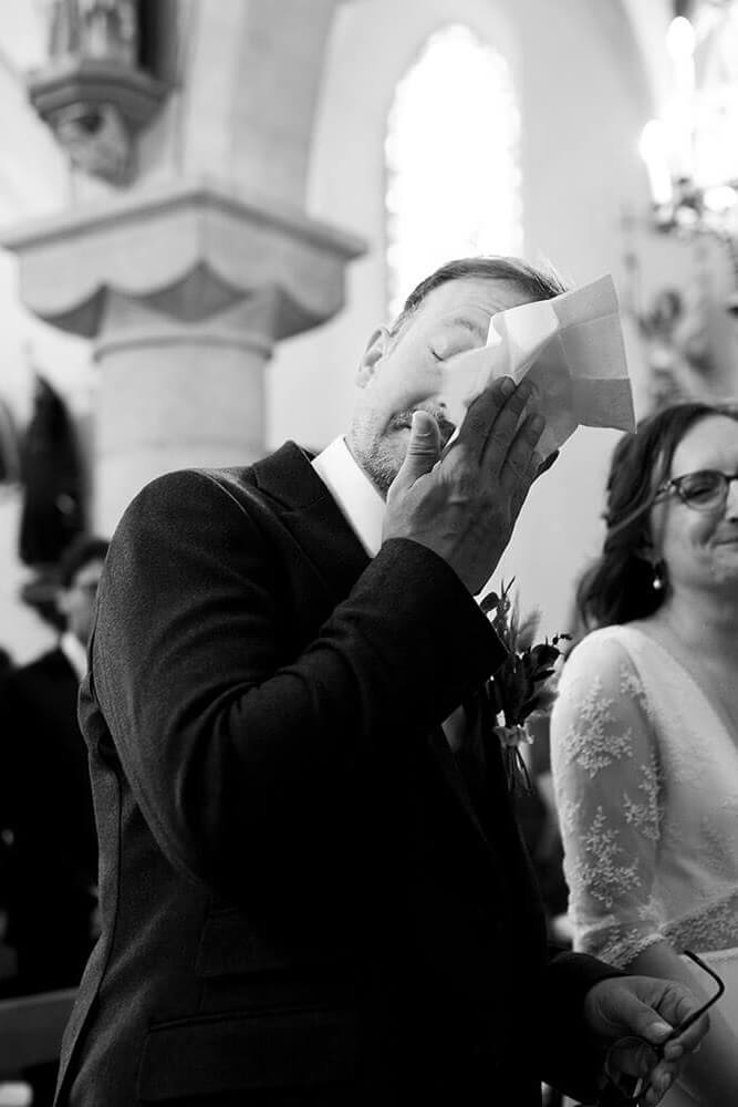 Pendant la cérémonie de mariage à l'église, le marié est très ému et fond en larmes. Il essuie ses larmes avec un mouchoir. Un moment fort en émotions capturé par Meyline Esparcieux, photographe de mariage dans les Landes, basée à Dax.