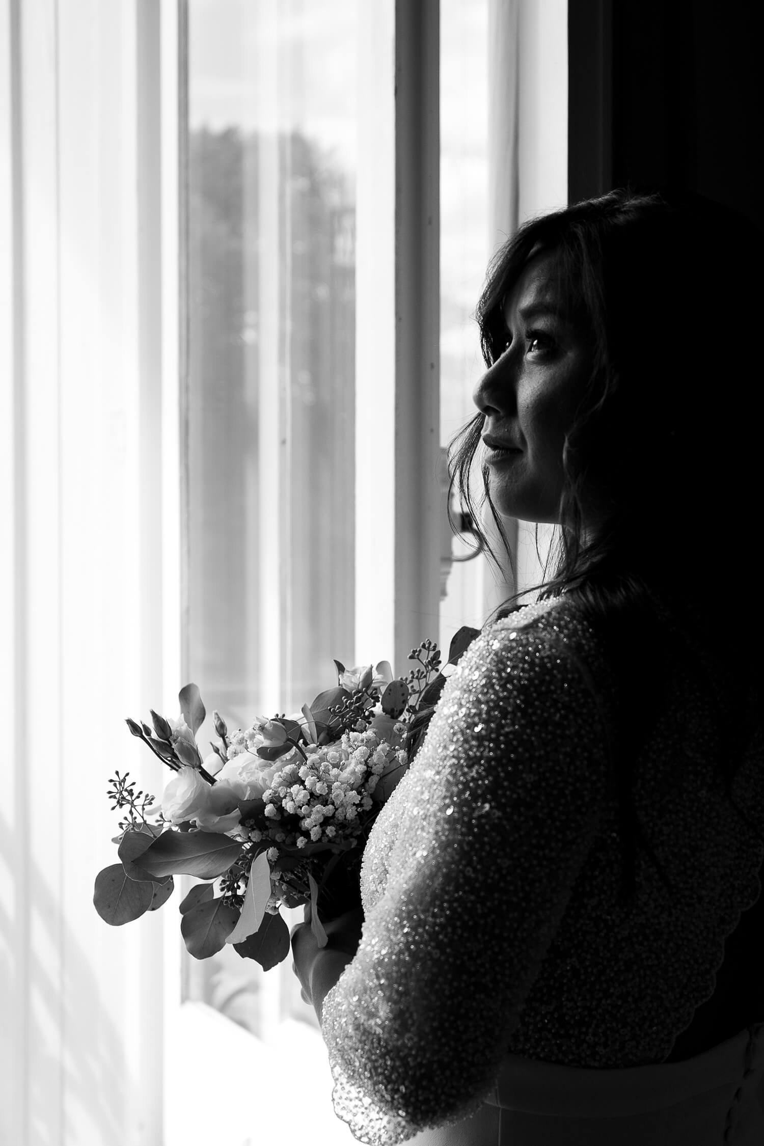 Une mariée regarde par la fenêtre à la fin de ses préparatifs. Un instant suspendu capturé par Meyline Esparcieux, photographe Dax.