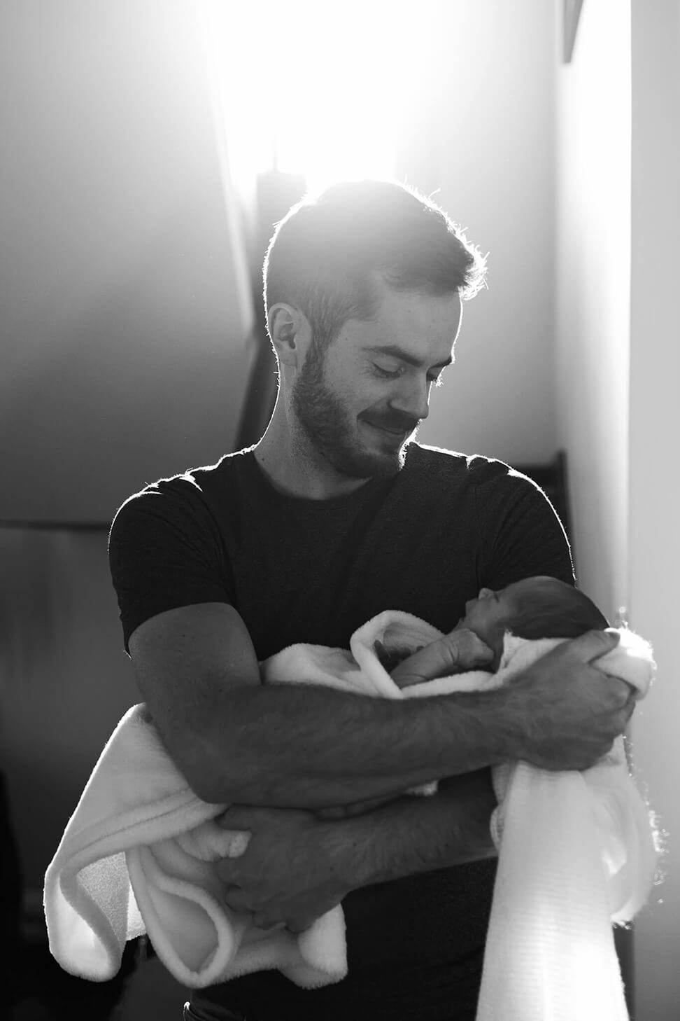 Un papa fier porte son bébé dans ses bras et le regarde avec amour. Un moment capté par Meyline Esparcieux, photographe Dax.