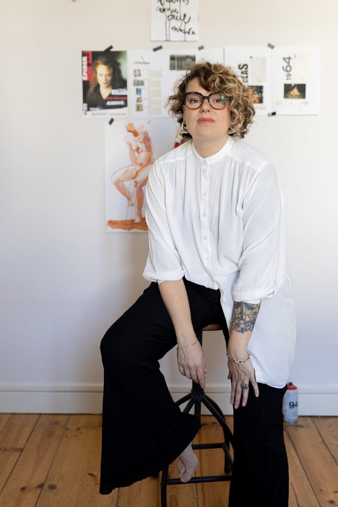 Elia Rolland, brand designer dans les Landes est assise sur un tabouret devant un moodboard de marque. Une photo prise lors de sa séance photo corporate à Dax.