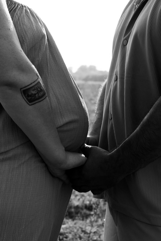 Le ventre rond de la femme enceinte contre son partenaire. Ils se tiennent les mains. Une séance grossesse réalisée par Meyline Esparcieux, photographe grossesse Dax Landes.